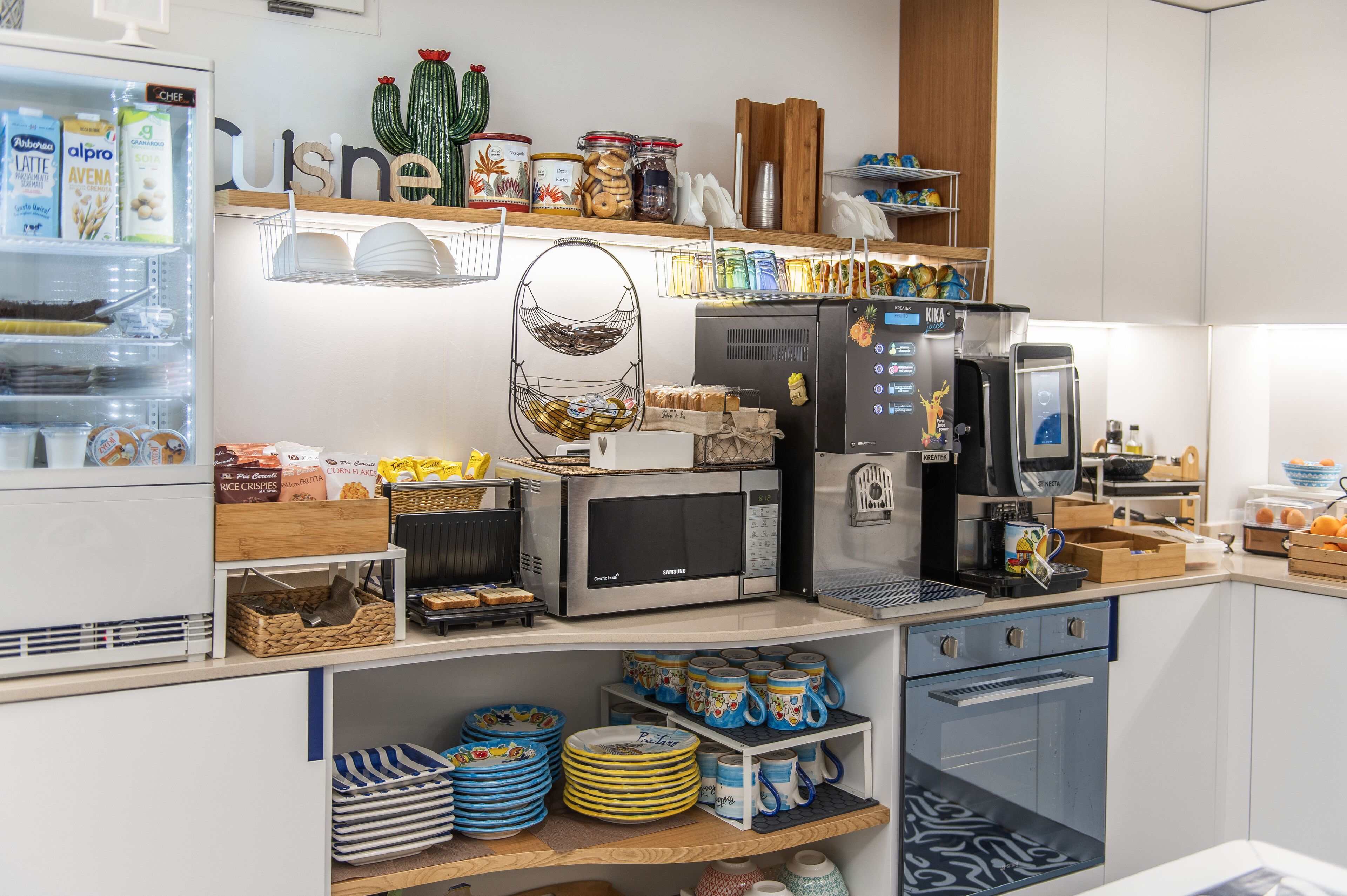 Una cocina equipada con refrigerador, microondas, cafetera y diversos utensilios y electrodomésticos.