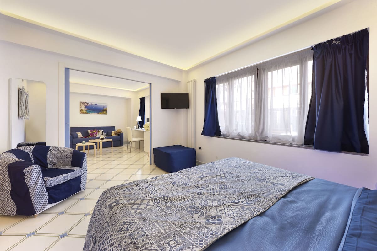 A modern hotel room with a large bed, a sofa, a small table, and a TV.