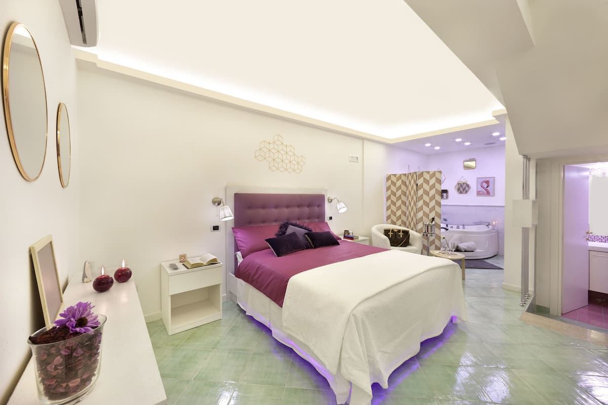 A modern bedroom with a large bed, bedside tables, a vanity, and a bathroom visible through an open door.