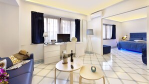 Een moderne hotelkamer met een zithoek, een bed met een blauwe hoofdbord, en een kleine tafel met een lamp.
