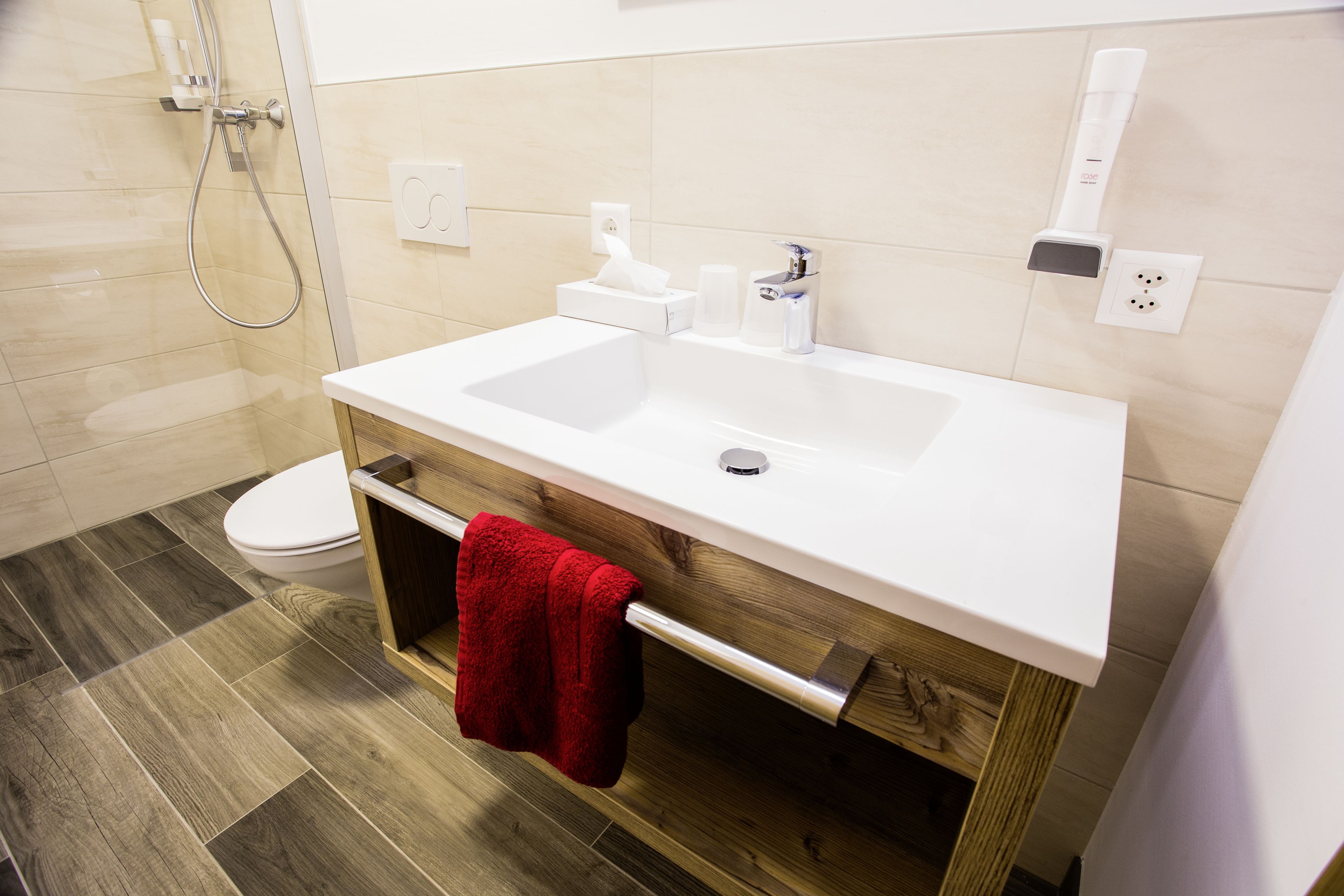 A modern bathroom with a white sink, wooden vanity, and a red towel.