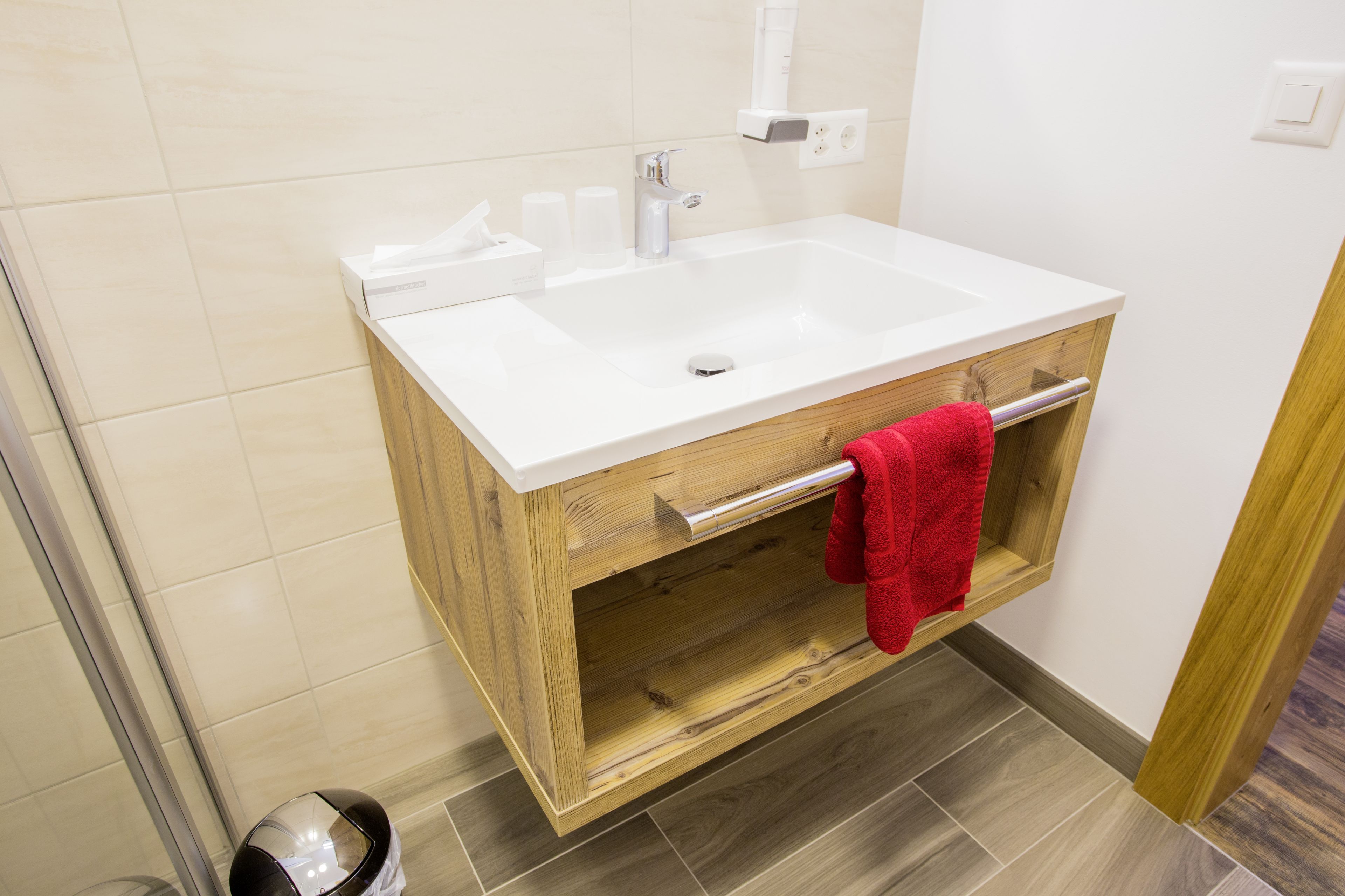 Une salle de bain avec un lavabo blanc, un meuble-lavabo en bois et une serviette rouge suspendue à un porte-serviettes.