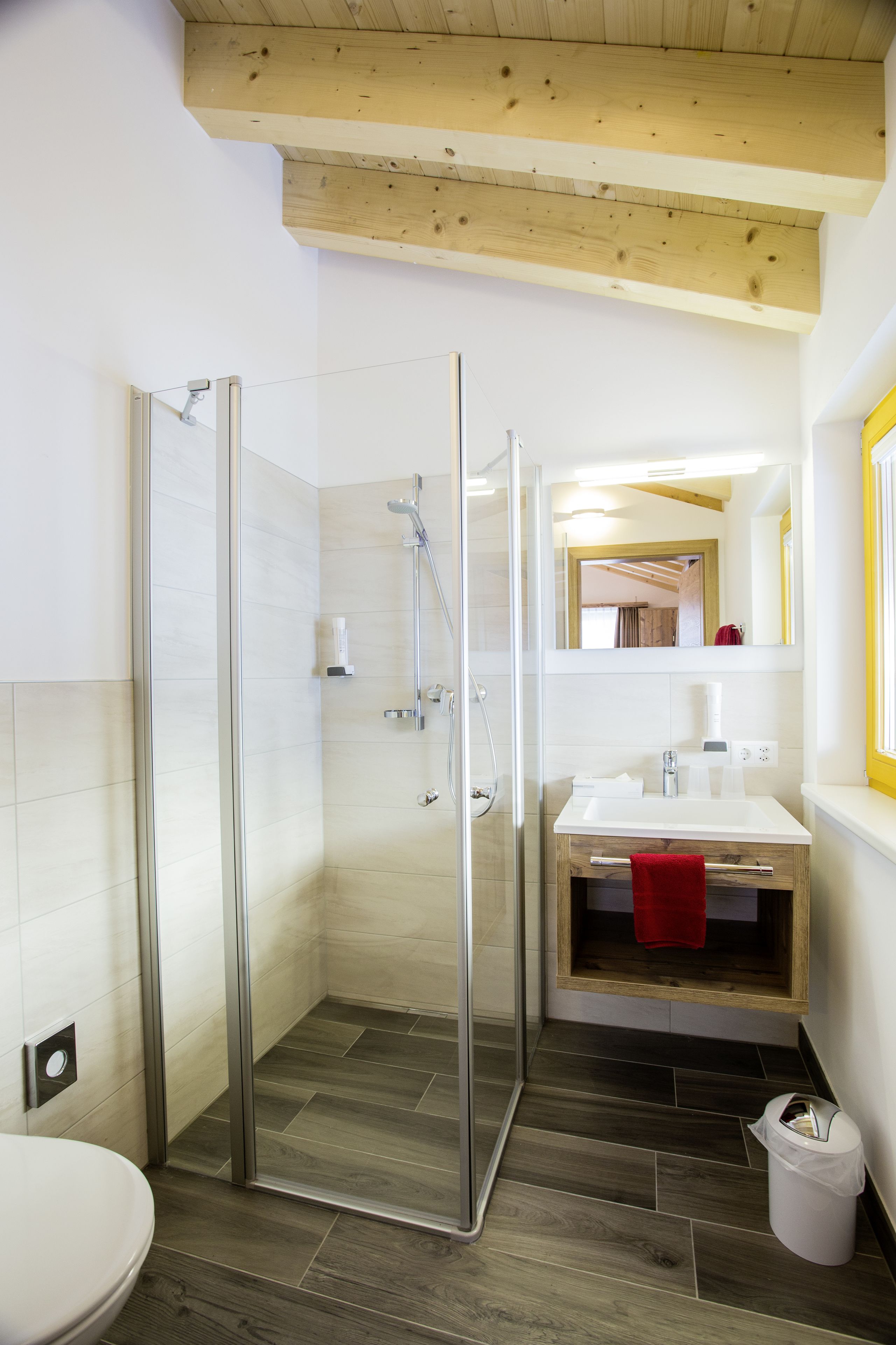 A modern bathroom with a glass shower enclosure, a white sink, and a wooden vanity.