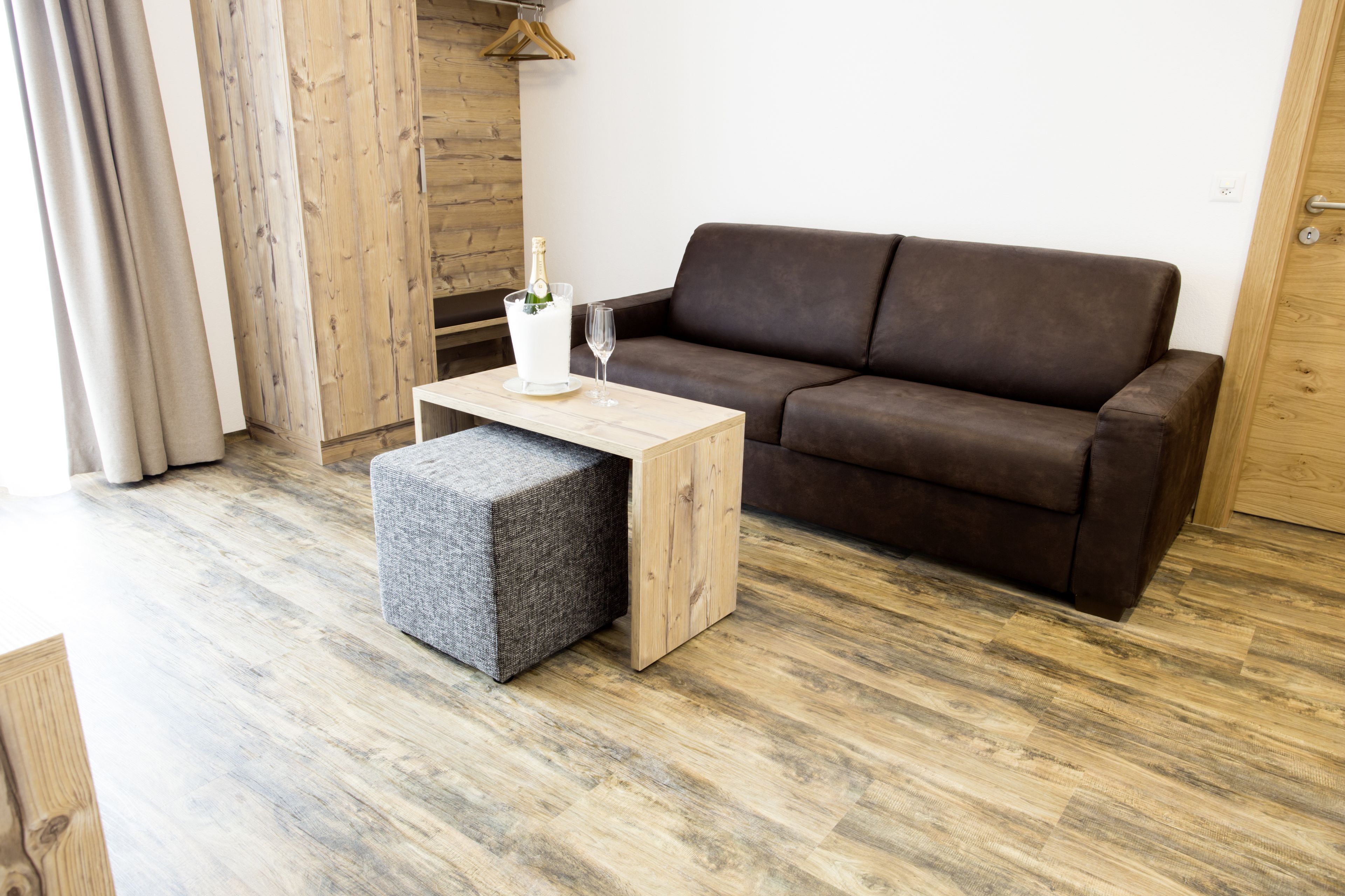 A modern living room with a brown sofa, a wooden coffee table, and a grey ottoman.