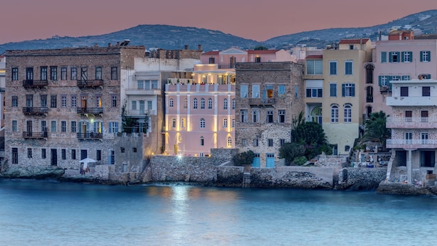 A coastal town with historic buildings along the waterfront, stone walls, and a clear view of the sea. - Apollonion Palace Hotel (Syros)