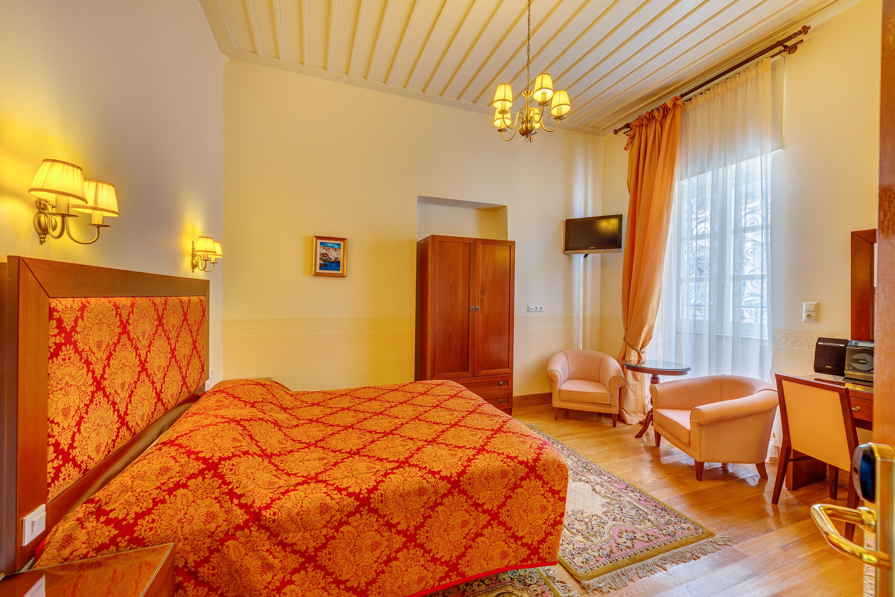 A hotel room with a bed, a desk, a chair, a TV, and a wardrobe.
