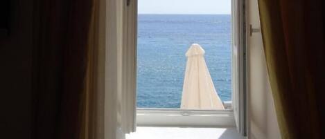 An open window with a view of the sea and a white umbrella outside.