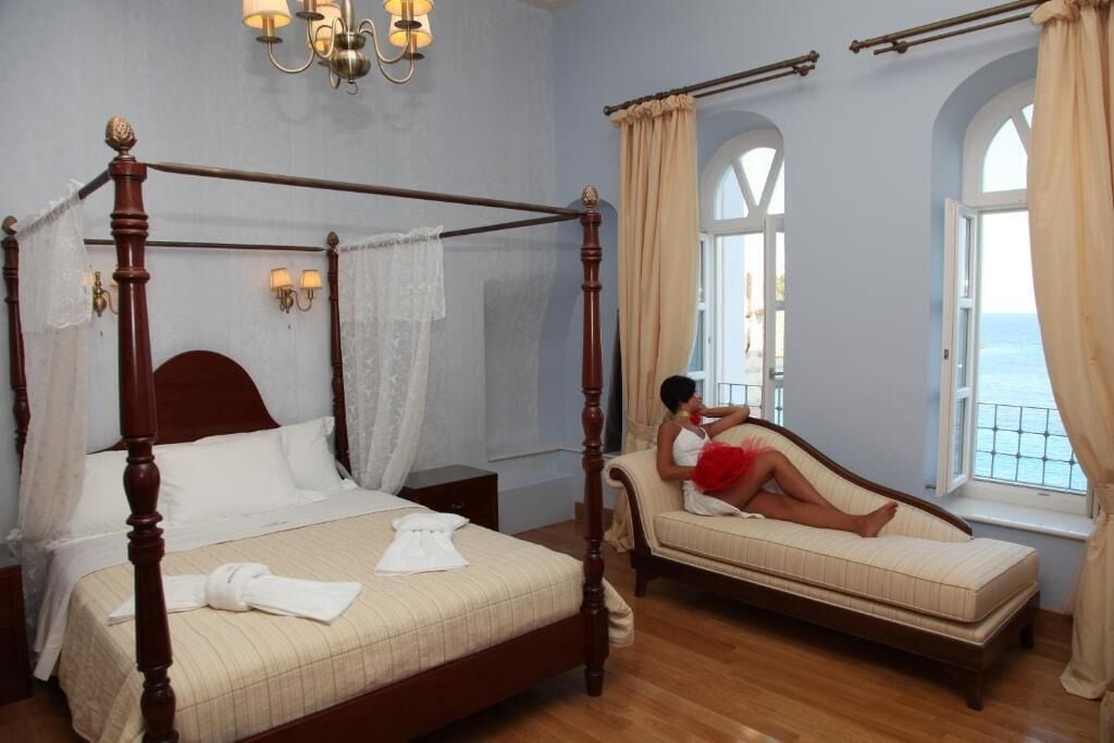 A four-poster bed with a canopy, a daybed, and a view of the sea through arched windows.