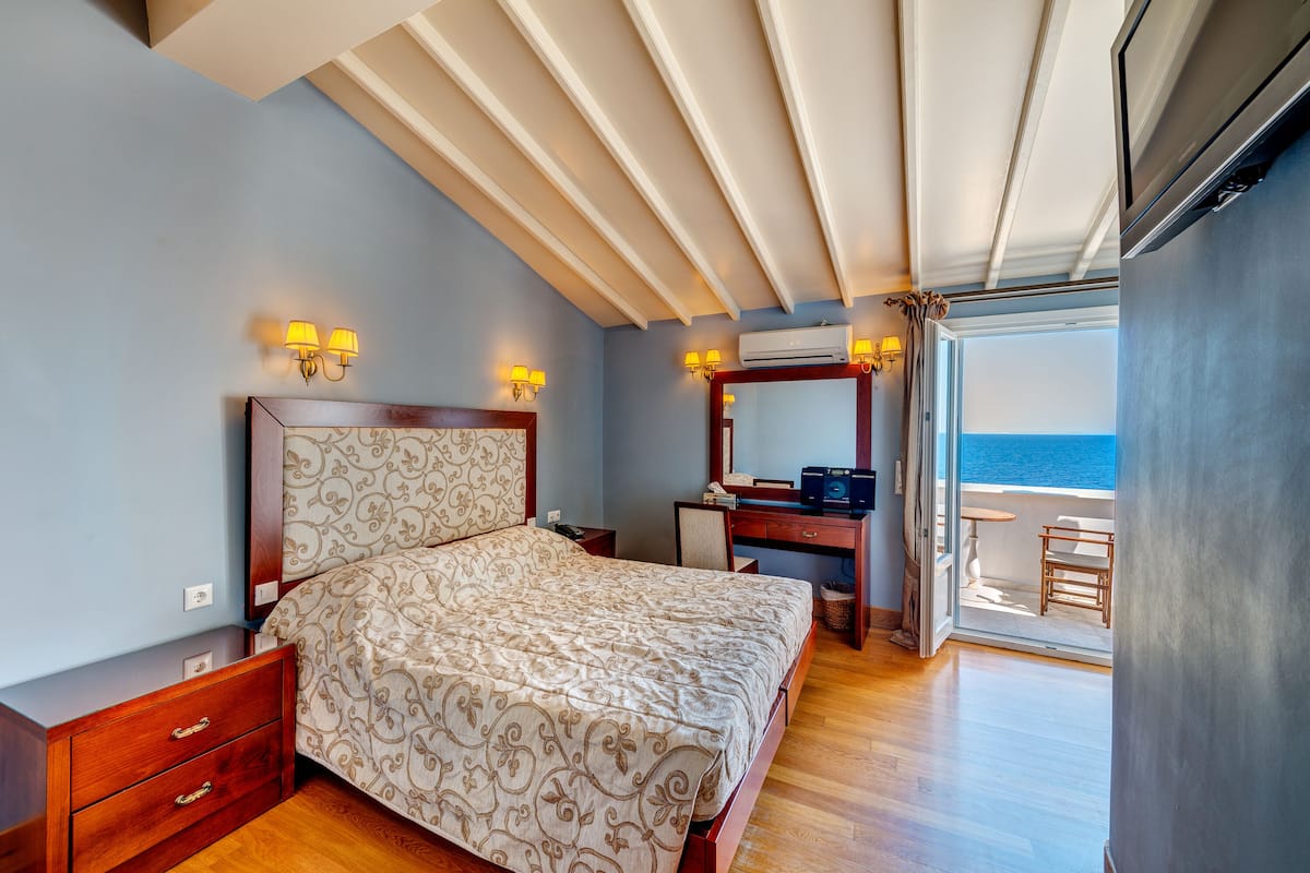 A bedroom with a bed, a desk, and a view of the sea.