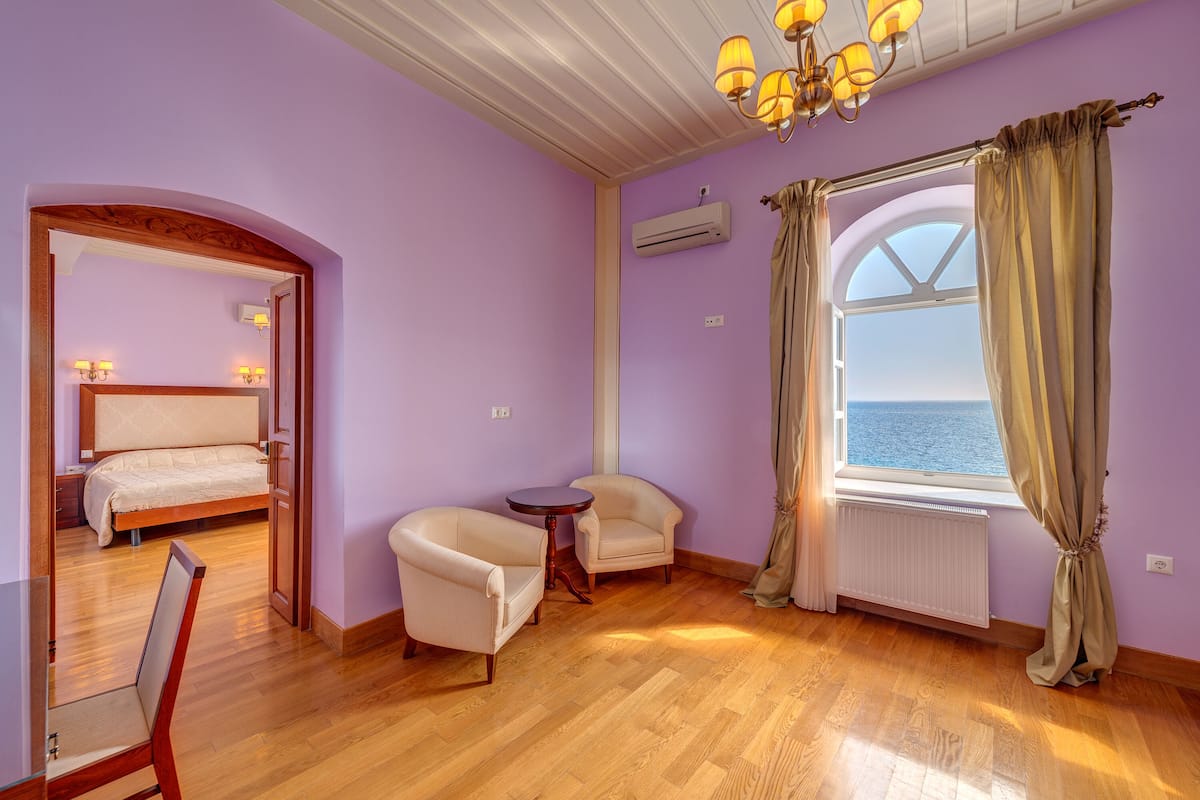 A room with a bed, two armchairs, a small table, a window with curtains, and a chandelier.
