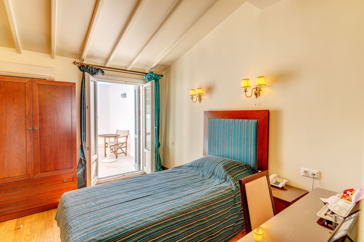 A hotel room with a bed, a wooden wardrobe, a desk with a telephone, and a window with curtains.
