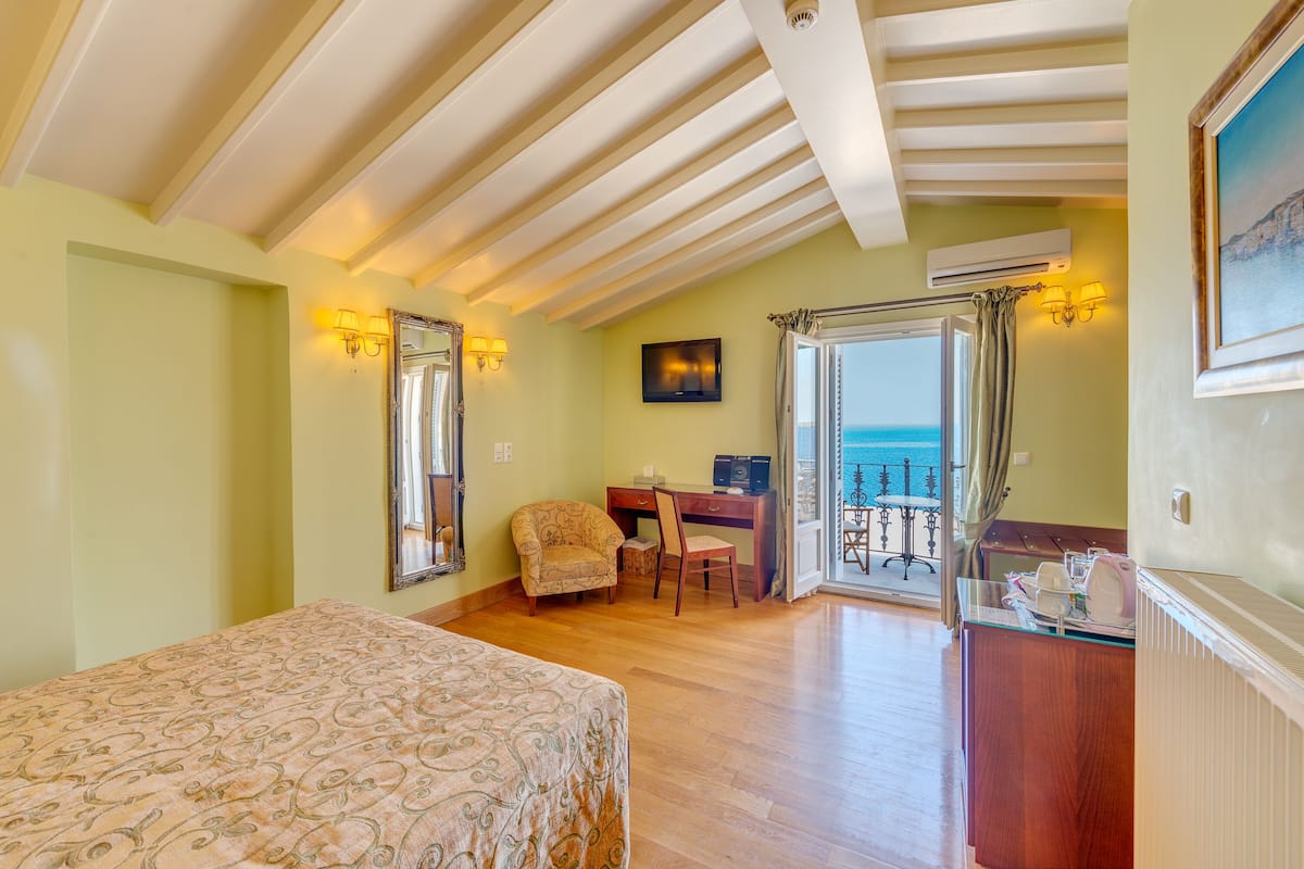 Un dormitorio con cama, escritorio, silla y vista al mar a través de una puerta de vidrio.