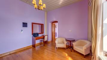 A room with wooden flooring, a desk with a chair, a sofa, and a chandelier.