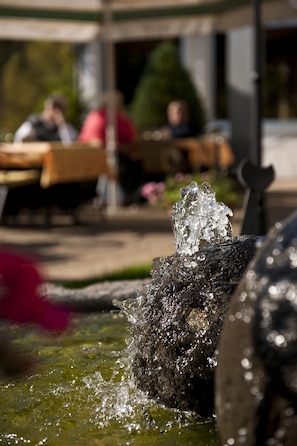 Una fuente con agua que cae sobre rocas, rodeada por un área de comedor con mesas y sillas.
