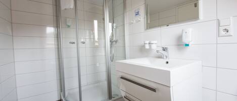 Un baño moderno con cabina de ducha de vidrio, un lavamanos blanco y un espejo encima.