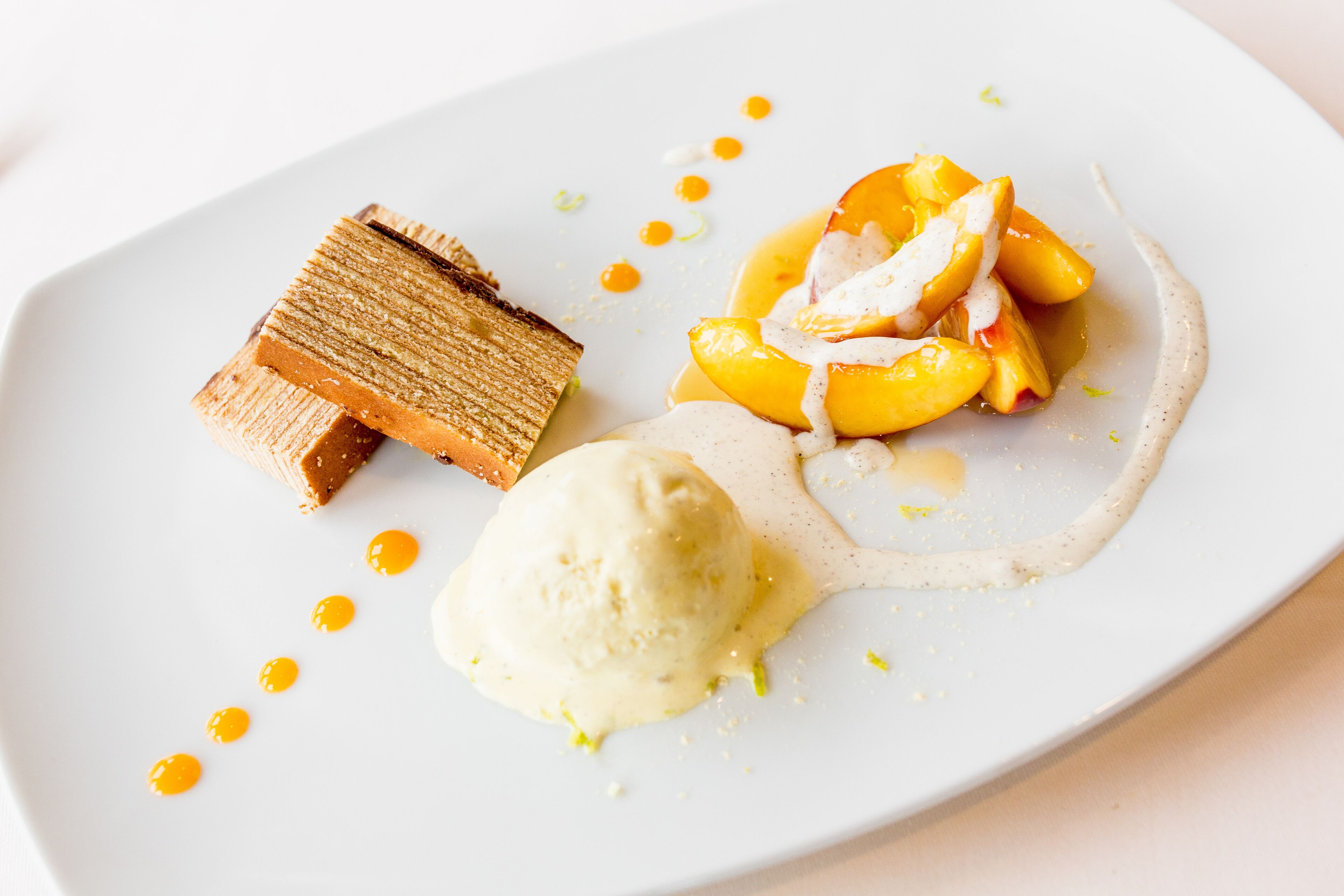 A dessert plate with a slice of cake, peach slices, and a scoop of ice cream.