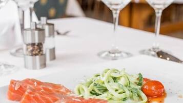Un plato blanco con salmón, espagueti de calabacín y tomates cherry sobre una mesa de restaurante.