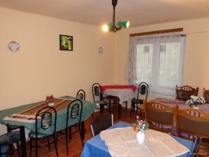 A dining area with two tables, chairs, a chandelier, a window with curtains, and a wall-mounted picture.