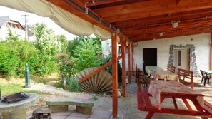 An outdoor patio with wooden tables and benches, surrounded by a garden with a large fan and a stone wall.