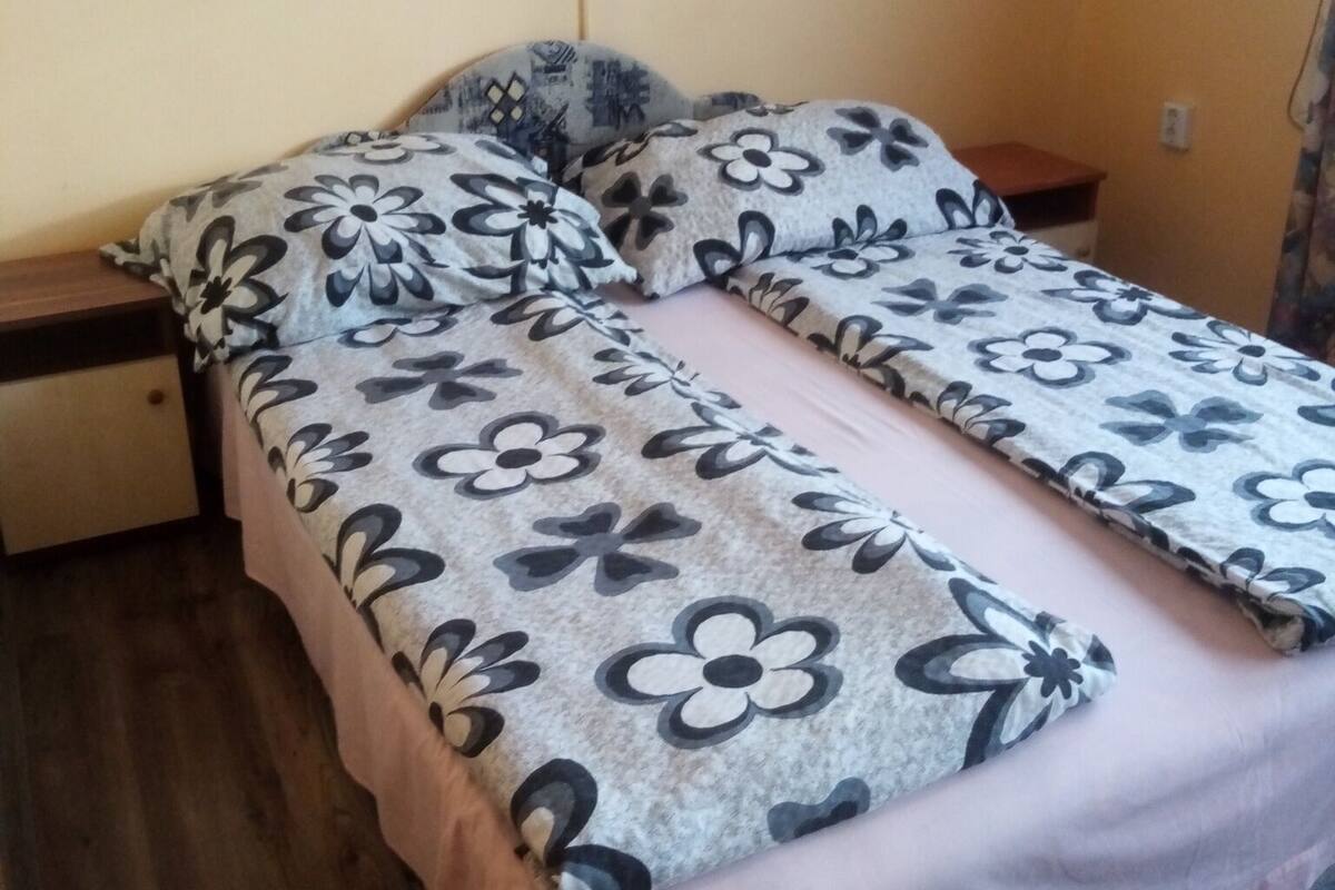 A single bed with a floral bedspread, a wooden nightstand, and a wall-mounted lamp.