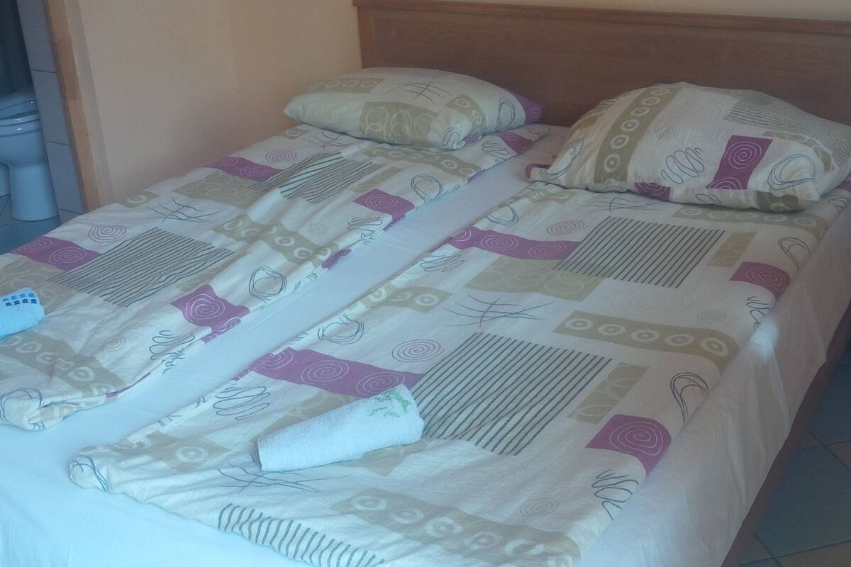 A bed with a patterned bedspread and pillows, a wooden headboard, and a tiled floor.
