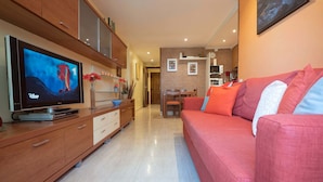 A modern living room with a flat-screen TV, wooden cabinets, a red sofa, and a dining area in the background. - Apartamento Els Cards (Sant Pere de Ribes)