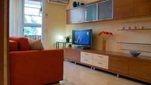 A modern living room with a red sofa, a television, and a cabinet with glass shelves. - Apartamento Els Cards (Sant Pere de Ribes)