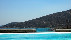 A pool area with clear blue water, a stone wall, and a mountainous backdrop. - Magganari View Villa - Discover Ultimate Summer Happiness! (Magganari Ios Island)
