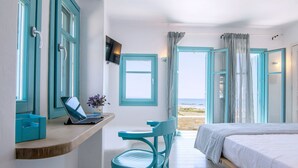A bedroom with a bed, a desk with a laptop, a chair, and a view of the beach through open doors. - Magganari View Villa - Discover Ultimate Summer Happiness! (Magganari Ios Island)
