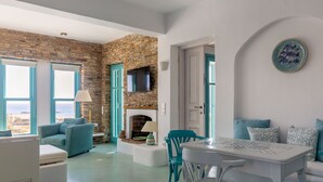 A modern living room with a stone wall, a fireplace, teal furniture, and a view of the sea. - Magganari View Villa - Discover Ultimate Summer Happiness! (Magganari Ios Island)