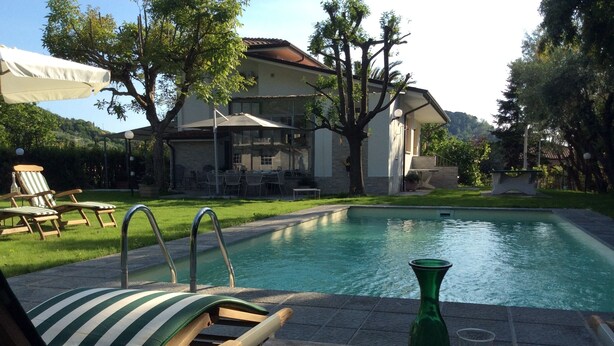 Une piscine entourée d’arbres et d’un bâtiment, avec des chaises longues et une table à proximité.