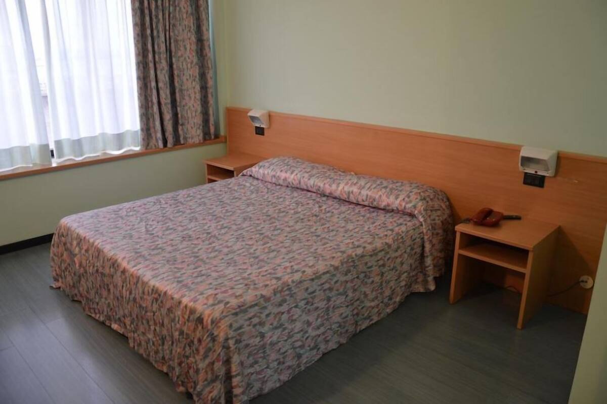 Ein Einzelbett mit floraler Bettdecke, Nachttische und ein Fenster mit Vorhängen.