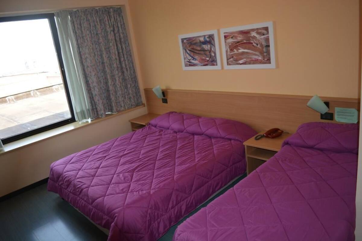 Ein Hotelzimmer mit zwei Betten, einem Fenster mit Vorhängen und zwei abstrakten Bildern an der Wand.