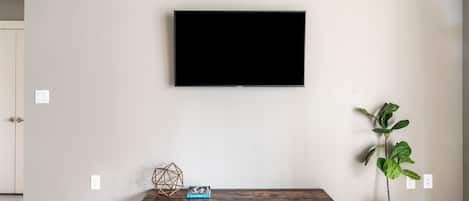 Un salon moderne avec un téléviseur fixé au mur, un banc en bois agrémenté d’objets décoratifs et une plante en pot.