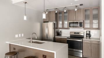 Una cocina moderna con una isla central, electrodomésticos de acero inoxidable, armarios de madera e iluminación colgante.