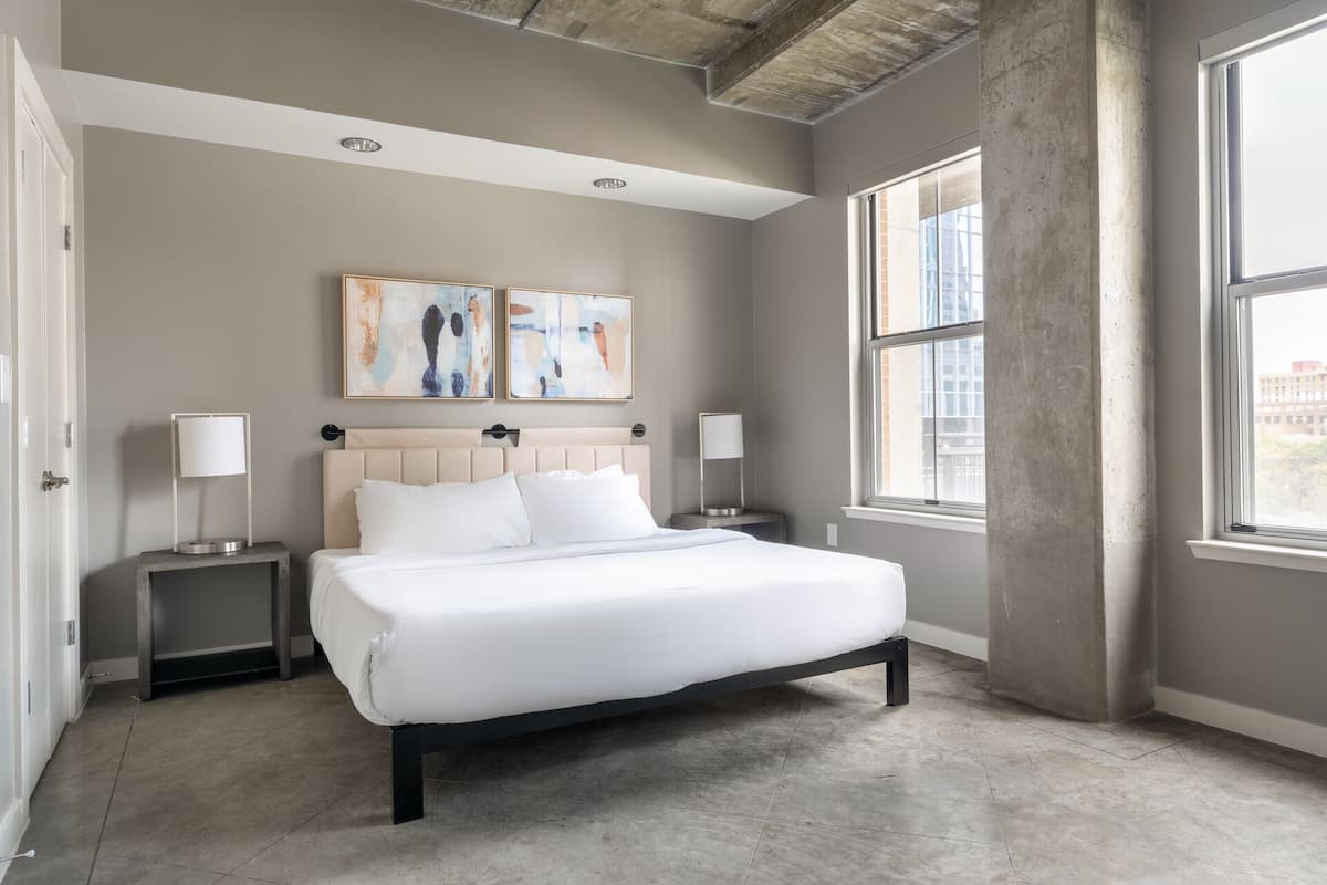 A modern bedroom with a large bed, two bedside tables, abstract art on the wall, and large windows.