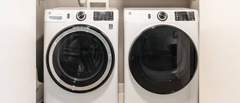 Dos lavadoras de carga frontal en un cuarto de lavado con una pared blanca y una tubería visible arriba.