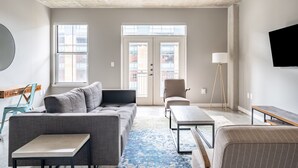 A modern living room with a grey sofa, a small table, a floor lamp, and a TV mounted on the wall. - Kasa Downtown Austin (Austin)