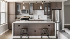 A modern kitchen with a central island, stainless steel appliances, and bar stools. - Kasa Downtown Austin (Austin)