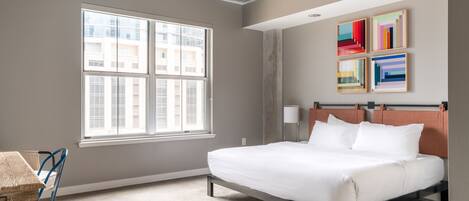 A modern hotel room with a large window, a bed, a desk, and a chair.