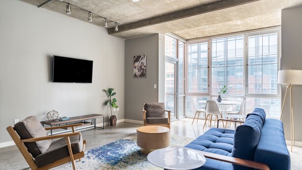 A modern living room with a blue sofa, a wooden coffee table, and a TV mounted on the wall. - Kasa Downtown Austin (Austin)