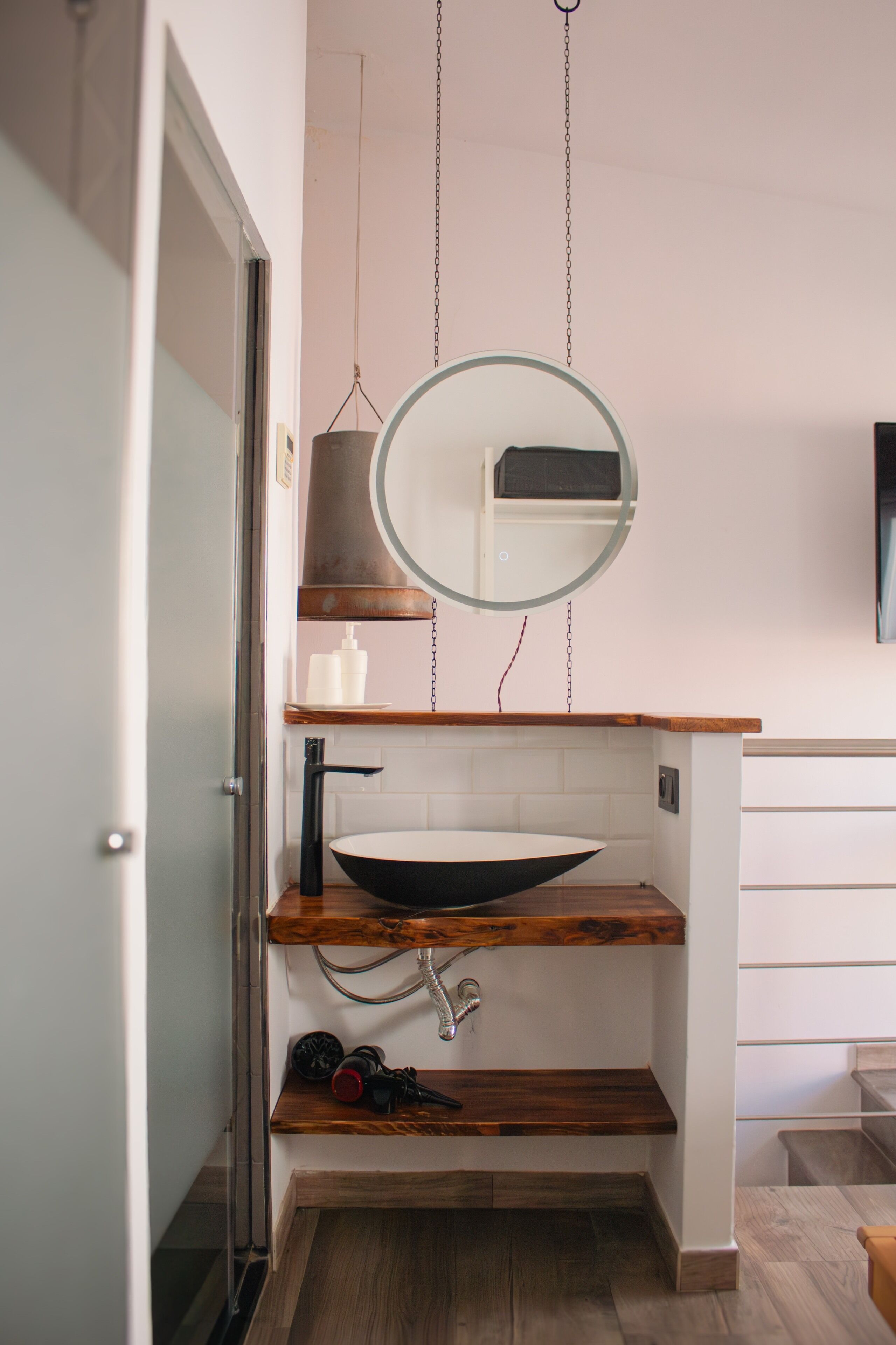 A modern bathroom with a wooden vanity, a round mirror, and a vessel sink.