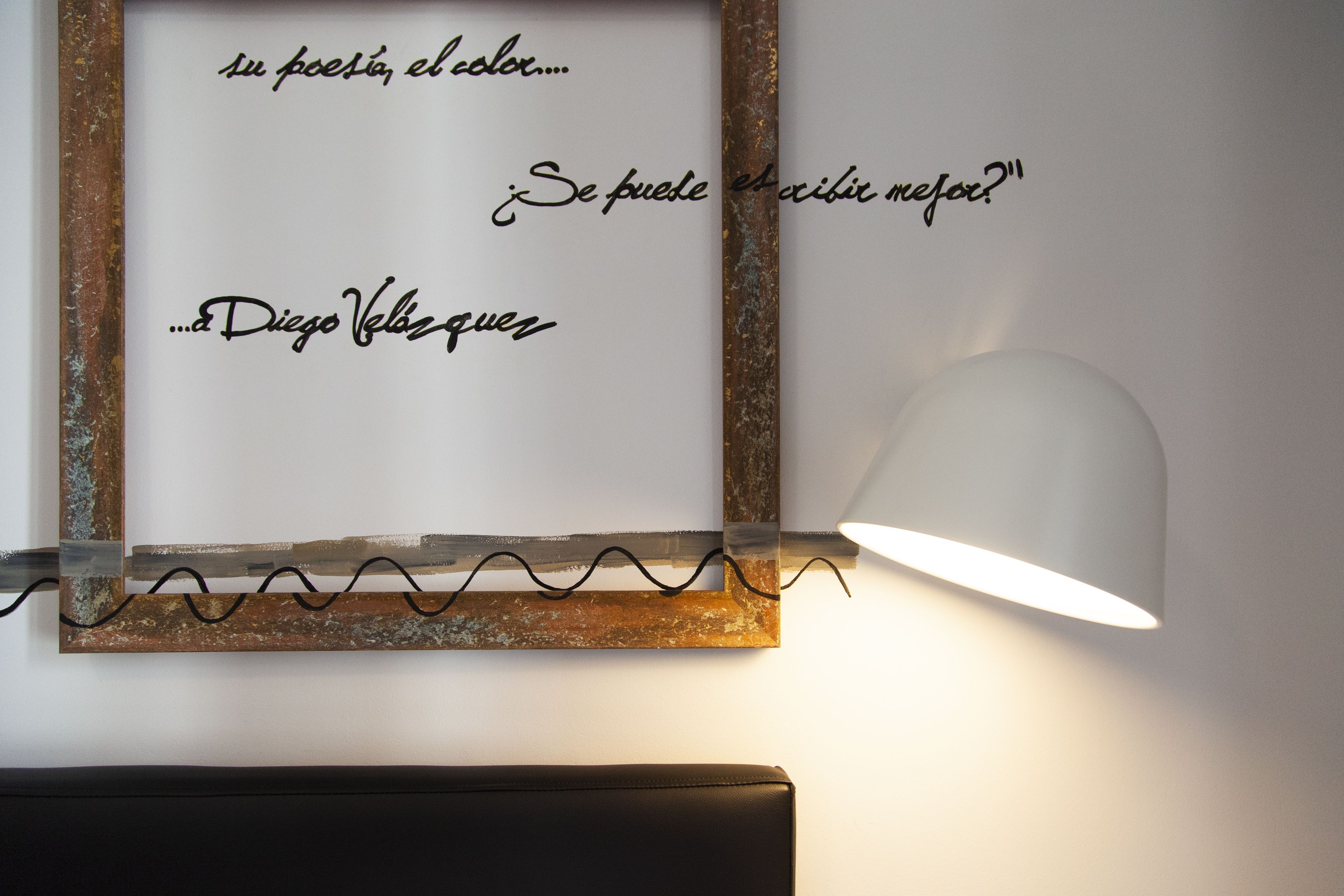 A framed quote on a wall with a lamp and a chair below.
