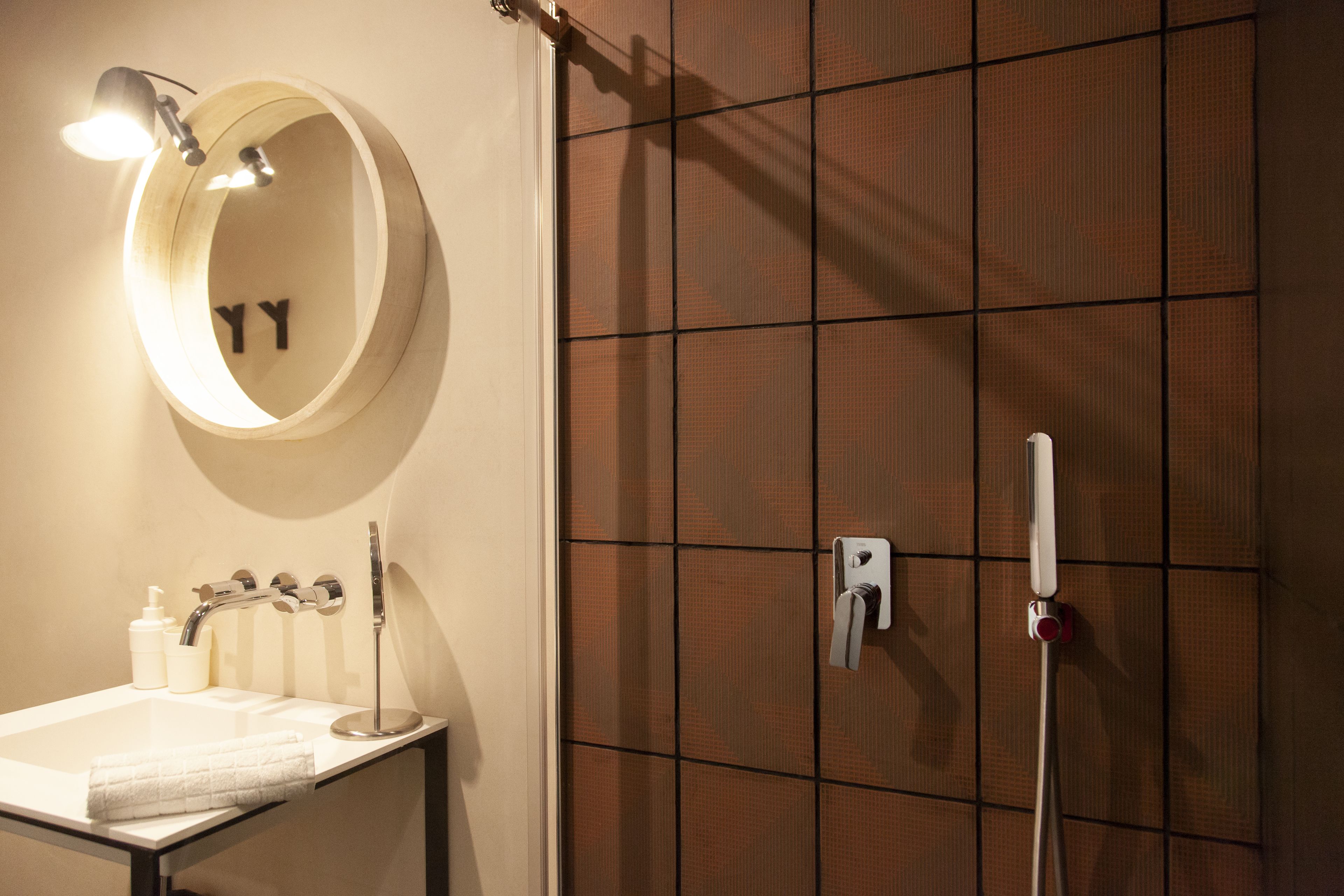 Un baño con espejo redondo, lavamanos, toalla, cabezal de ducha y secamanos.