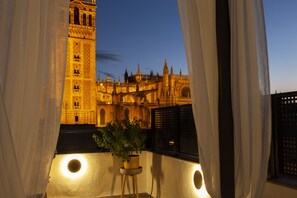 A balcony with a potted plant, a view of a historic building with a clock tower, and curtains partially drawn.