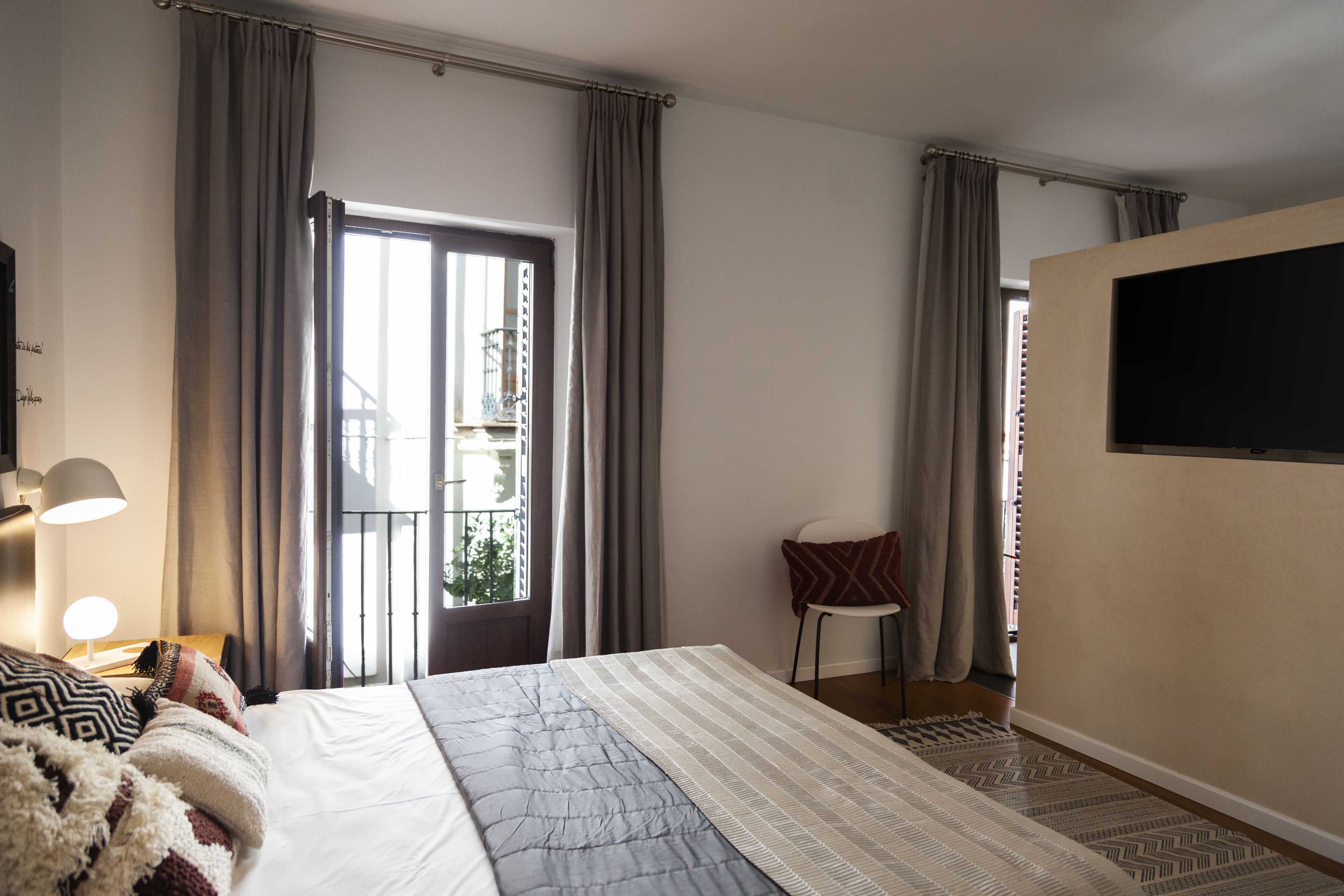 Een hotelkamer met een bed, een stoel, een televisie en een raam met gordijnen.
