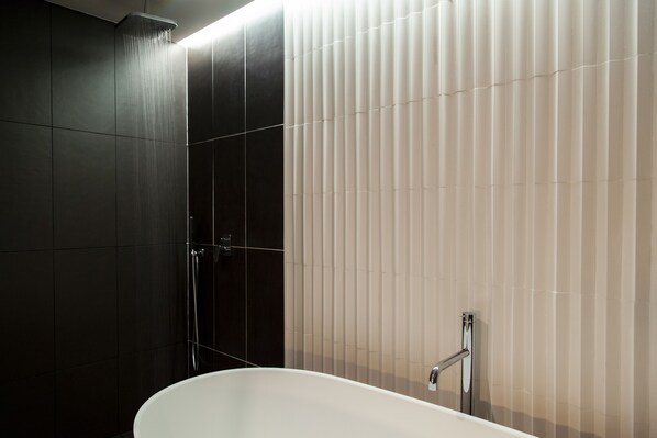 A modern bathroom with a freestanding bathtub, a shower area, and a wall with vertical blinds.