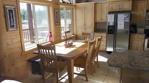 A wooden cabin with a dining table, chairs, a refrigerator, and a window with a fire extinguisher.