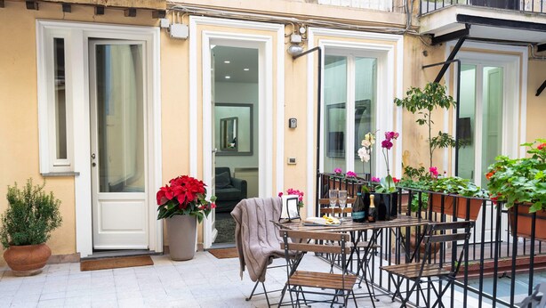 A patio with a table and chairs, potted plants, and a door leading to an interior space. - White Style Alcove - Piazza Di Spagna (Roma)