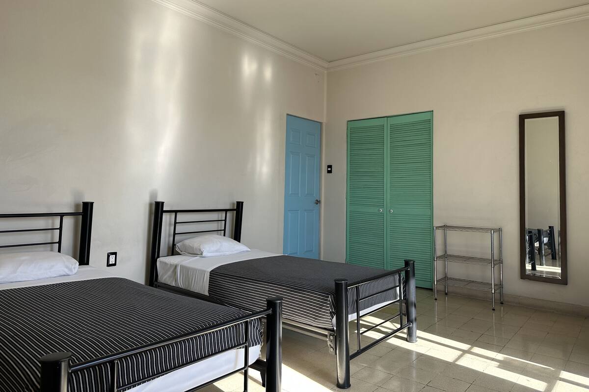 Une chambre avec deux lits, une porte bleue, une porte verte et un miroir.